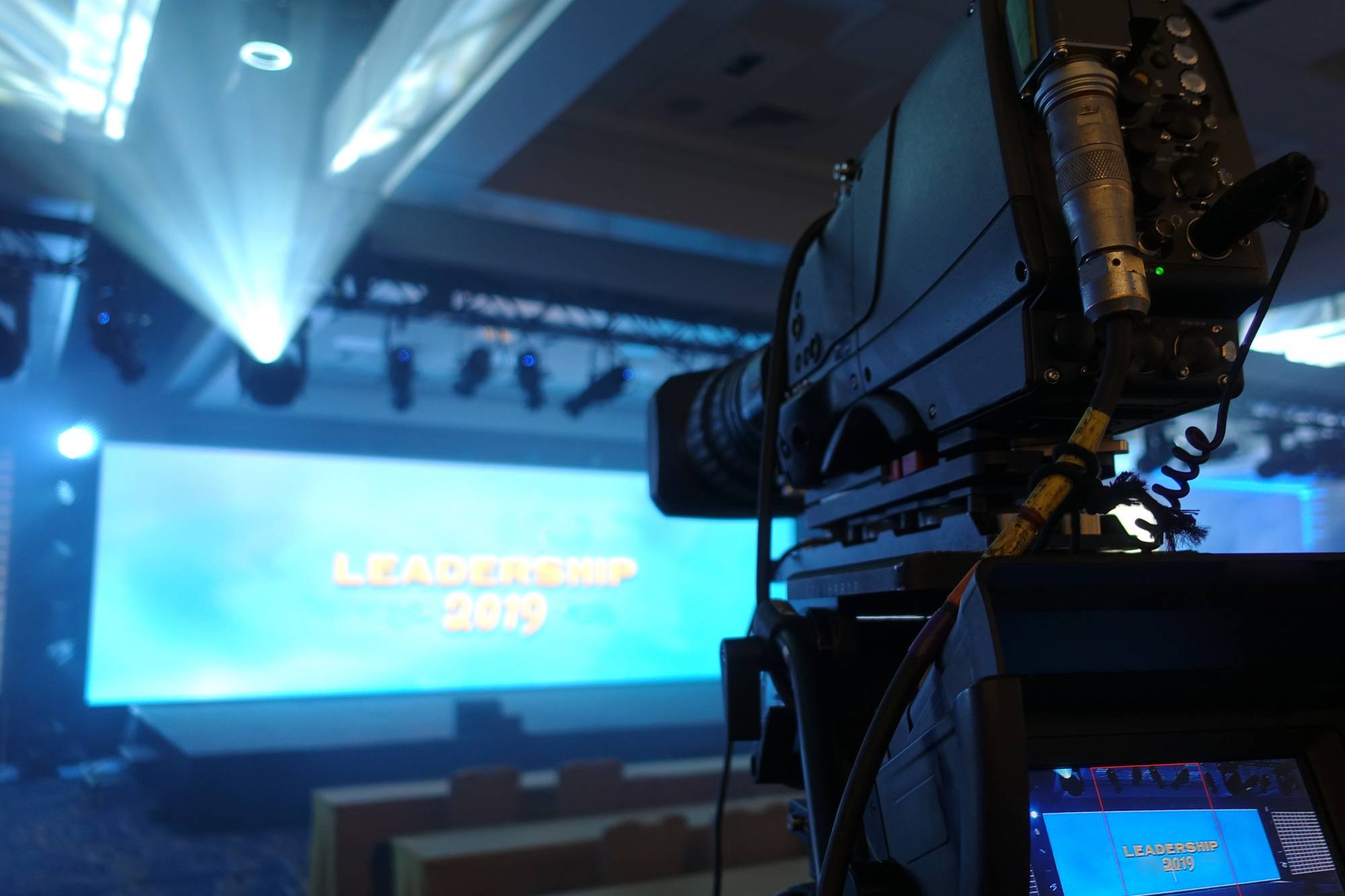 Professional video camera with long lens set up to shoot a corporate event, fog creates dramatic lighting effects